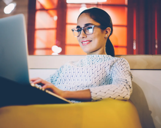 woman on the lounge with glasses looking at her laptop screen smiling